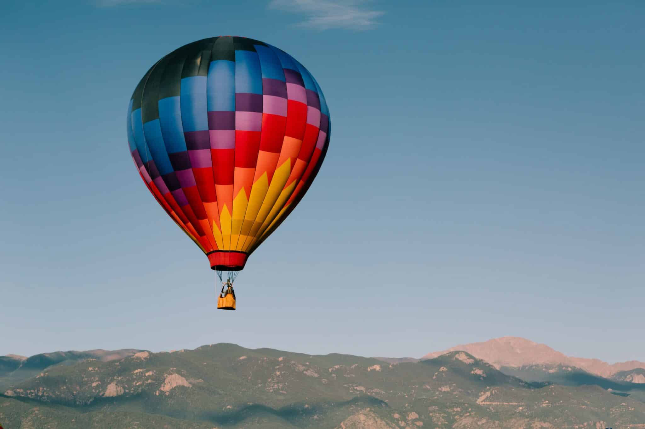 A single colorful hot air balloon floating above the Colorado Springs mountains near sober living homes.