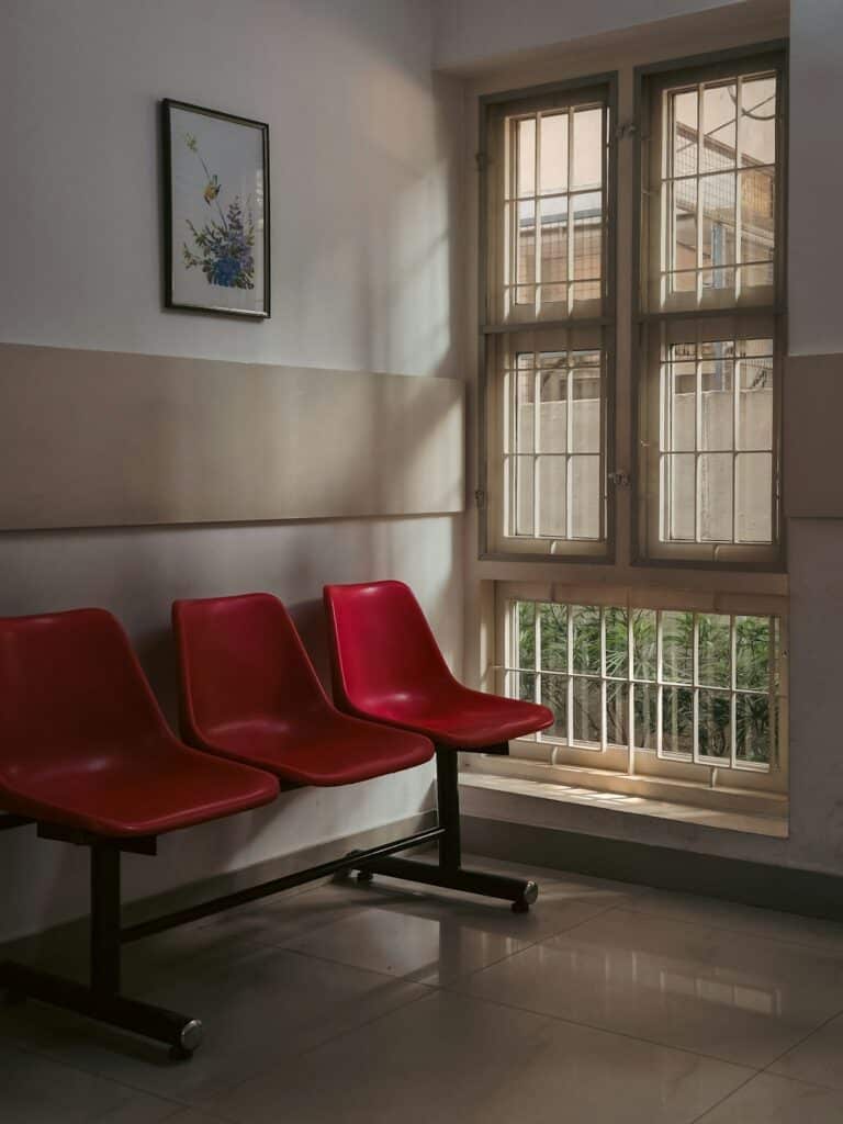 Three red chairs in a waiting room by window -- Photo by Adhitya Sibikumar on Unsplash