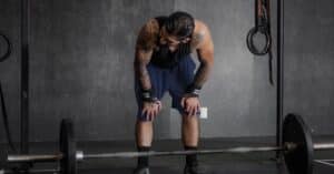 A muscular man with tattoos rests after an intense weightlifting session in the gym.