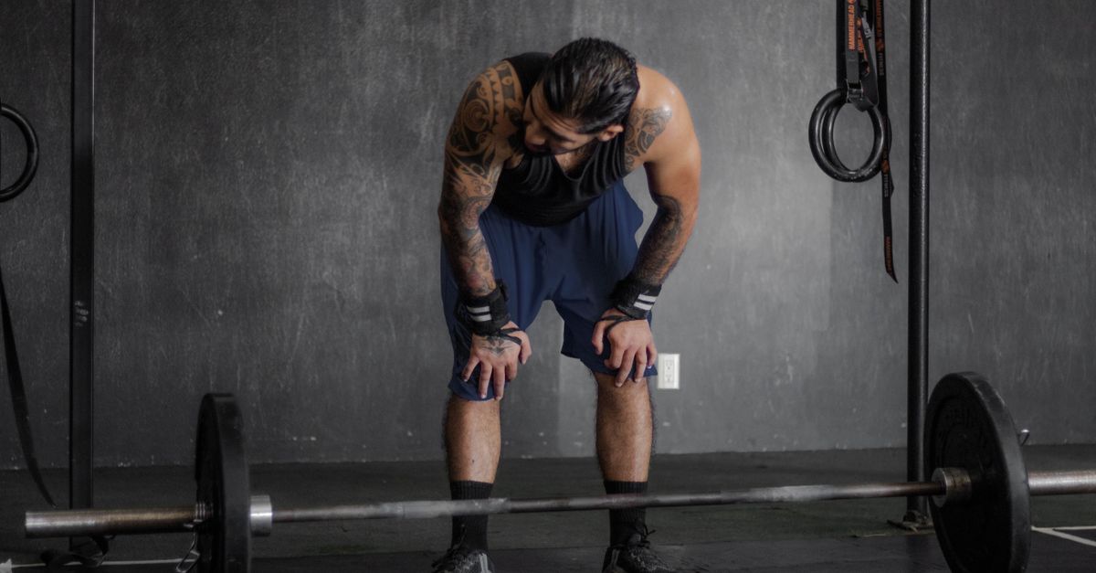 A muscular man with tattoos rests after an intense weightlifting session in the gym.