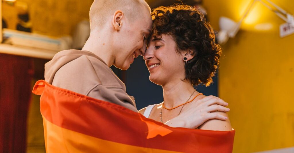 LGBTQ couple wrapped in a pride flag, sharing a warm and loving embrace indoors.