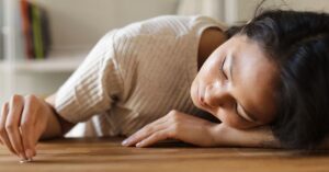 Woman lying on wooden table, appearing emotional, with a small object in hand.