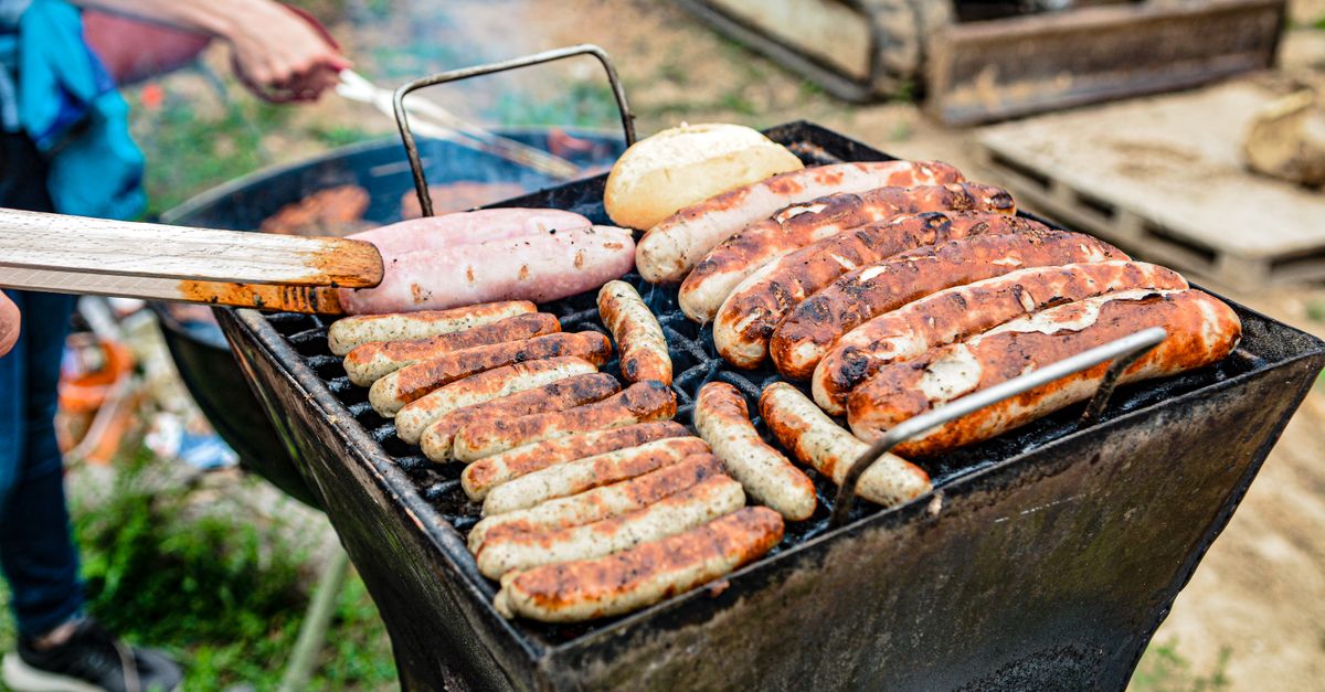 Grilling an assortment of sausages and bread at an outdoor barbecue on a sunny day.