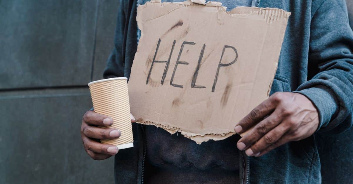 Close-up of a person holding a cardboard sign with 'Help' and a paper cup, representing need and assistance.