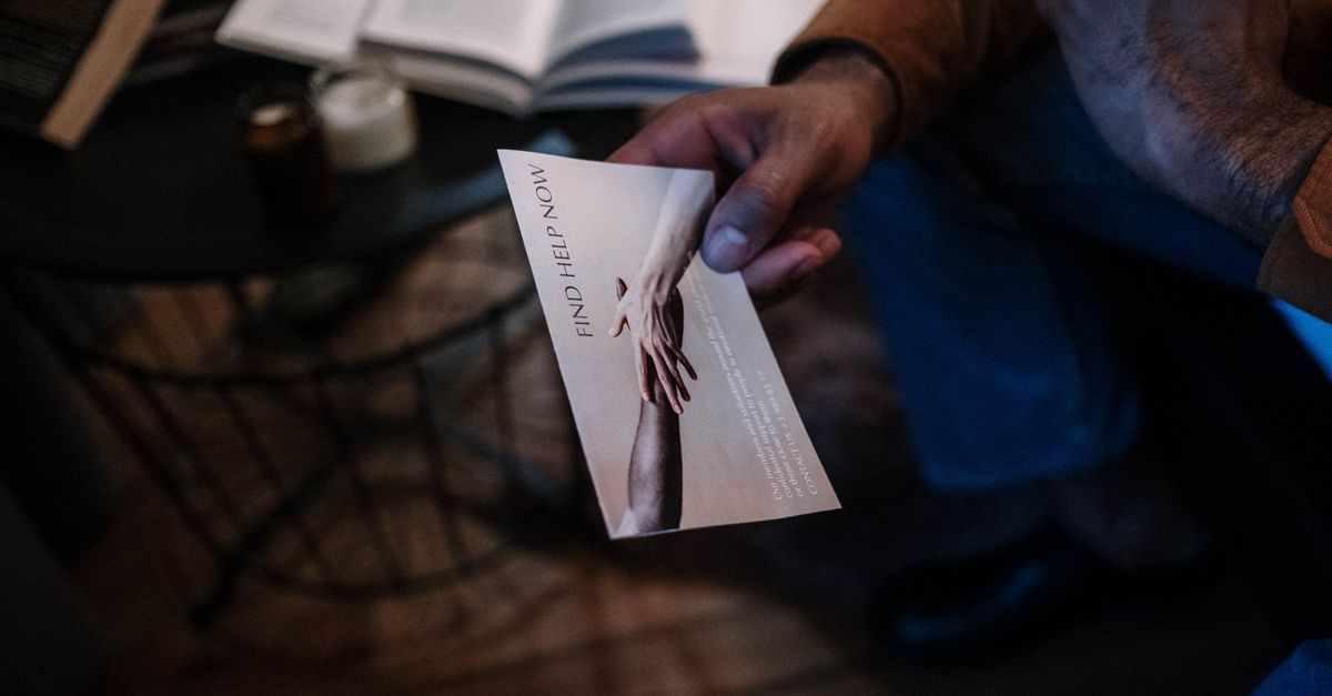 A person holds a help brochure in a cozy indoor setting, symbolizing support and mental health awareness.
