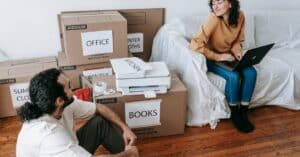 Young couple organizing boxes and relaxing with laptop during moving day indoors.