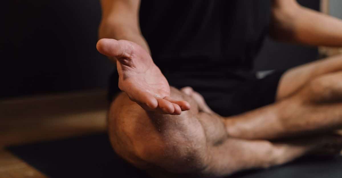 Crop unrecognizable barefoot male sitting with crossed legs on sports mat during stress relief meditation session