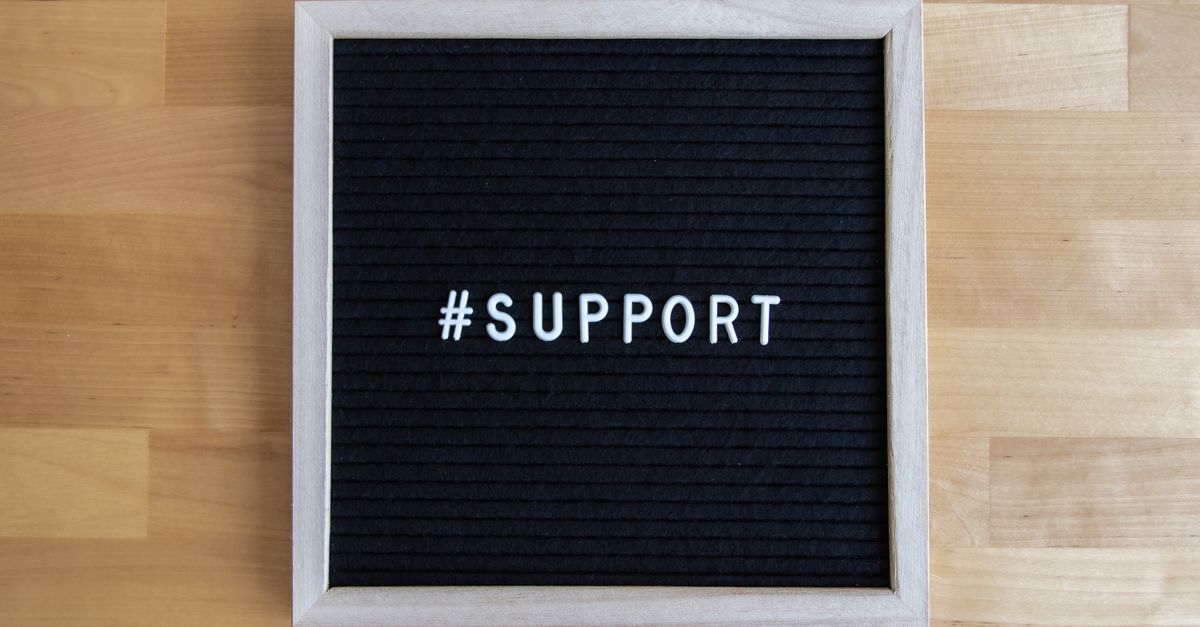 Black letter board displaying the word '#support' on a wooden table surface.