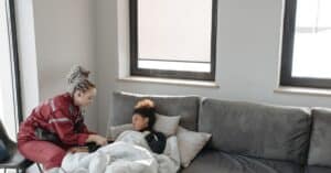 Emergency responder assisting a sick woman on a sofa indoors.