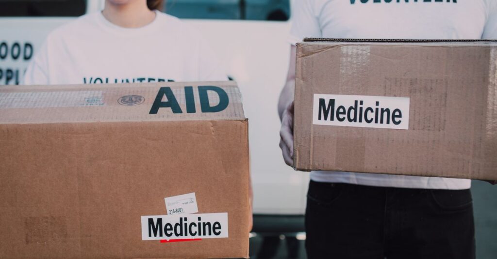 Volunteers holding boxes labeled 'AID' and 'Medicine', preparing donations.