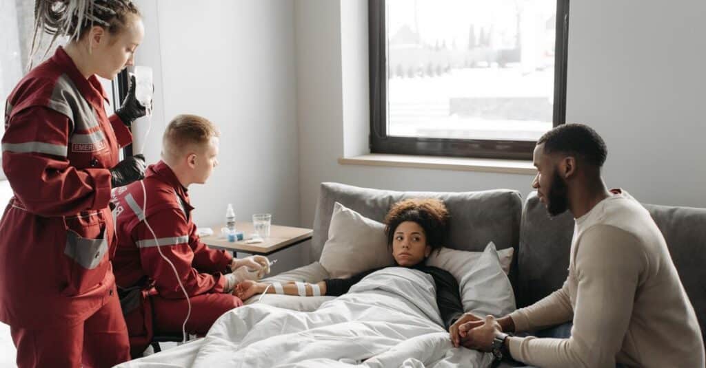 Paramedics provide care to a sick person at home, showcasing emergency medical assistance in a domestic setting.