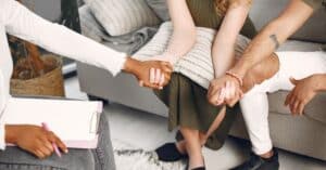 Diverse group holding hands on a couch during a therapy session.