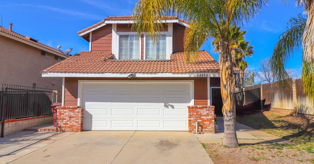 A sunlit suburban house with a garage and palm trees in the driveway.