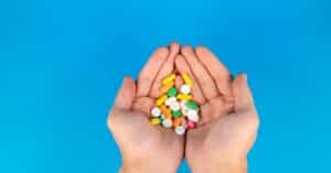 A pair of hands gently cradles a variety of colorful pills against a vibrant blue backdrop, symbolizing healthcare.