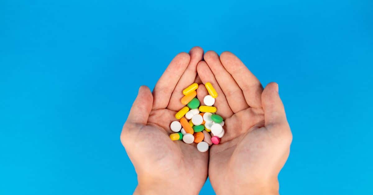 A pair of hands gently cradles a variety of colorful pills against a vibrant blue backdrop, symbolizing healthcare.