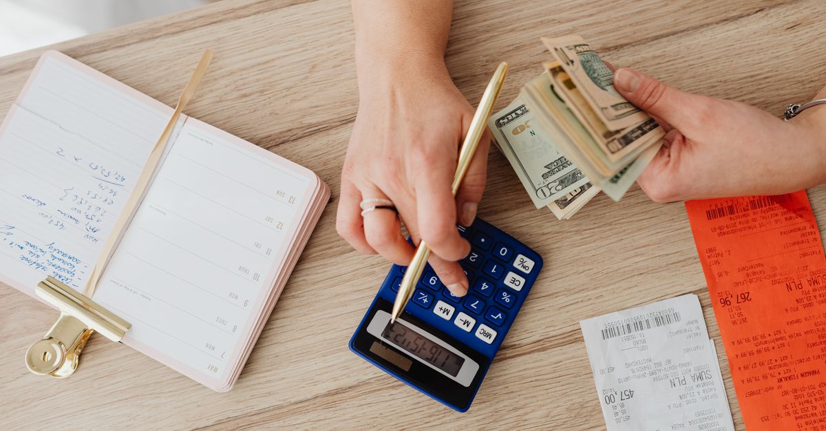 Hands managing finances with calculator, cash, and receipts on a wooden table. Ideal for budgeting concepts.