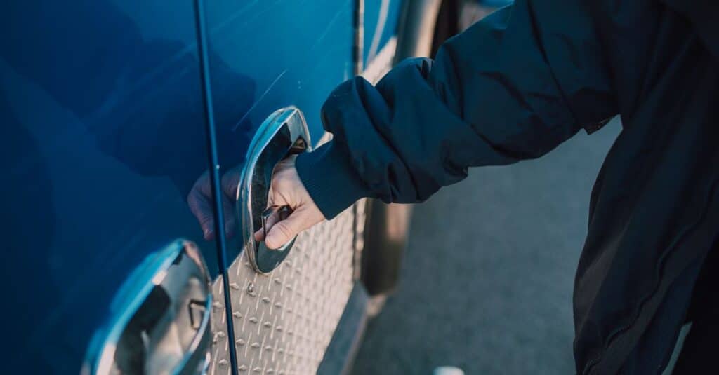 A person in a jacket opens a handle on a blue emergency vehicle, likely an ambulance.