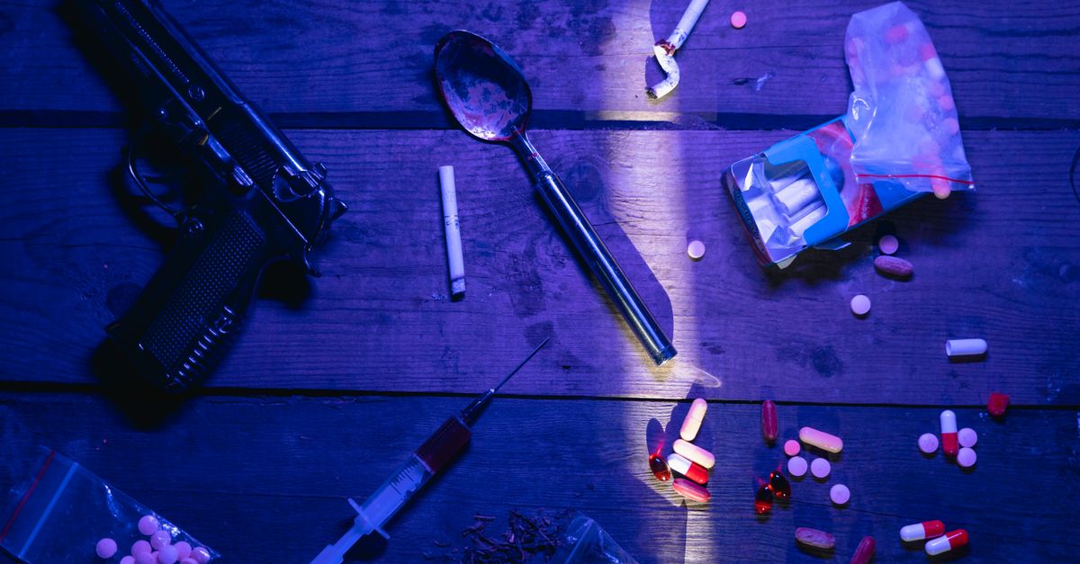 Intriguing still life image depicting pills, a gun, and syringe under dramatic lighting.