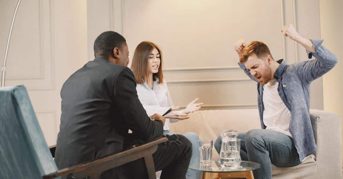 A couple engaging in a heated discussion during a therapy session with a therapist.