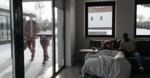Healthcare professionals approach a patient's home through snow, providing emergency care indoors.