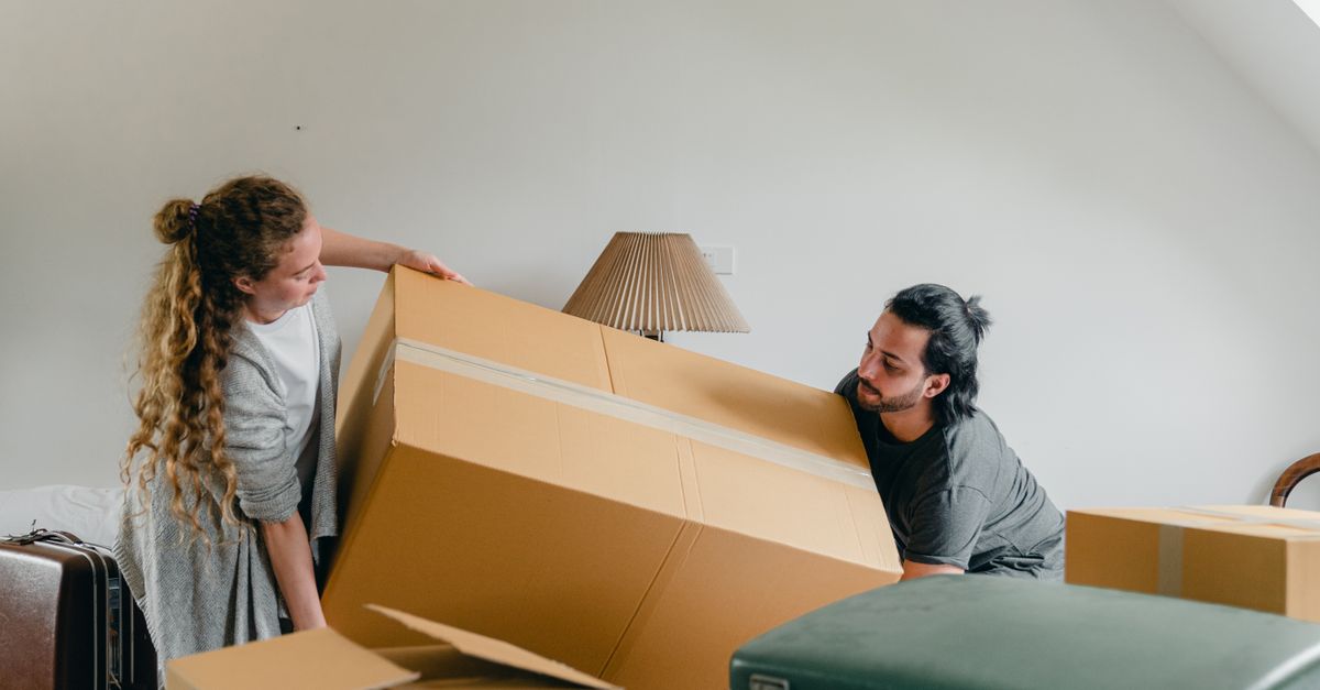 Serious male and female in casual wear carrying carton box while moving to new apartment