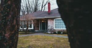 Exterior of suburban shabby brick house with large windows chimney and street lamp over entrance doorway and yard