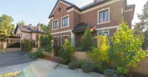 Elegant brick house with a lush garden and driveway, under a clear sky.