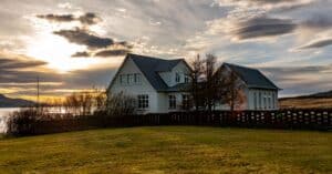 Idyllic countryside house near a calm lake during sunset, with stunning cloud patterns.