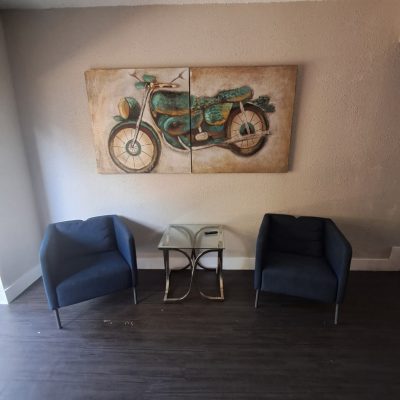 Two-man suite sober living Austin with blue chairs, motorcycle artwork, and glass side table