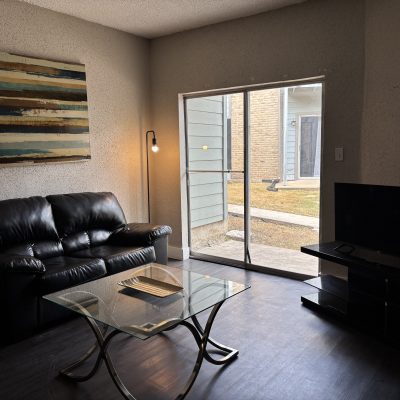 Modern living room in Austin sober living home with black leather couch, glass coffee table, and patio access