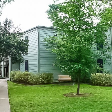 Exterior view of the apartment community with lawn, trees, sidewalk, and two-story buildings.