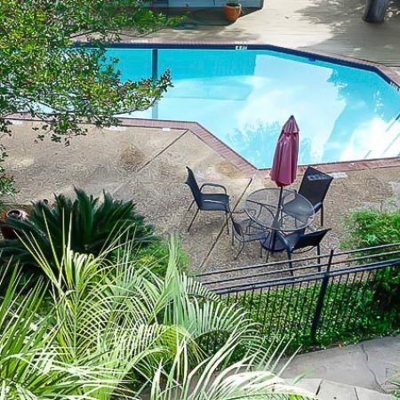Fenced swimming pool with patio table, chairs, umbrella, and surrounding landscaping.
