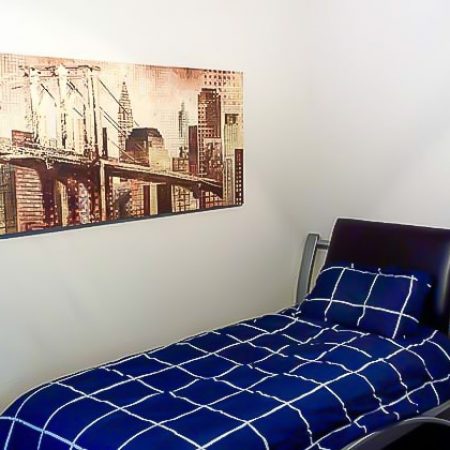 Single bed with blue bedding in a furnished bedroom with white walls and framed wall art.