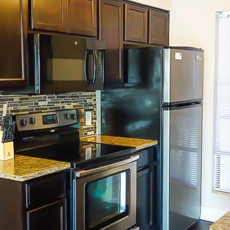 Shared apartment kitchen with dark wood cabinets, granite countertops, stainless steel stove, microwave, and refrigerator.